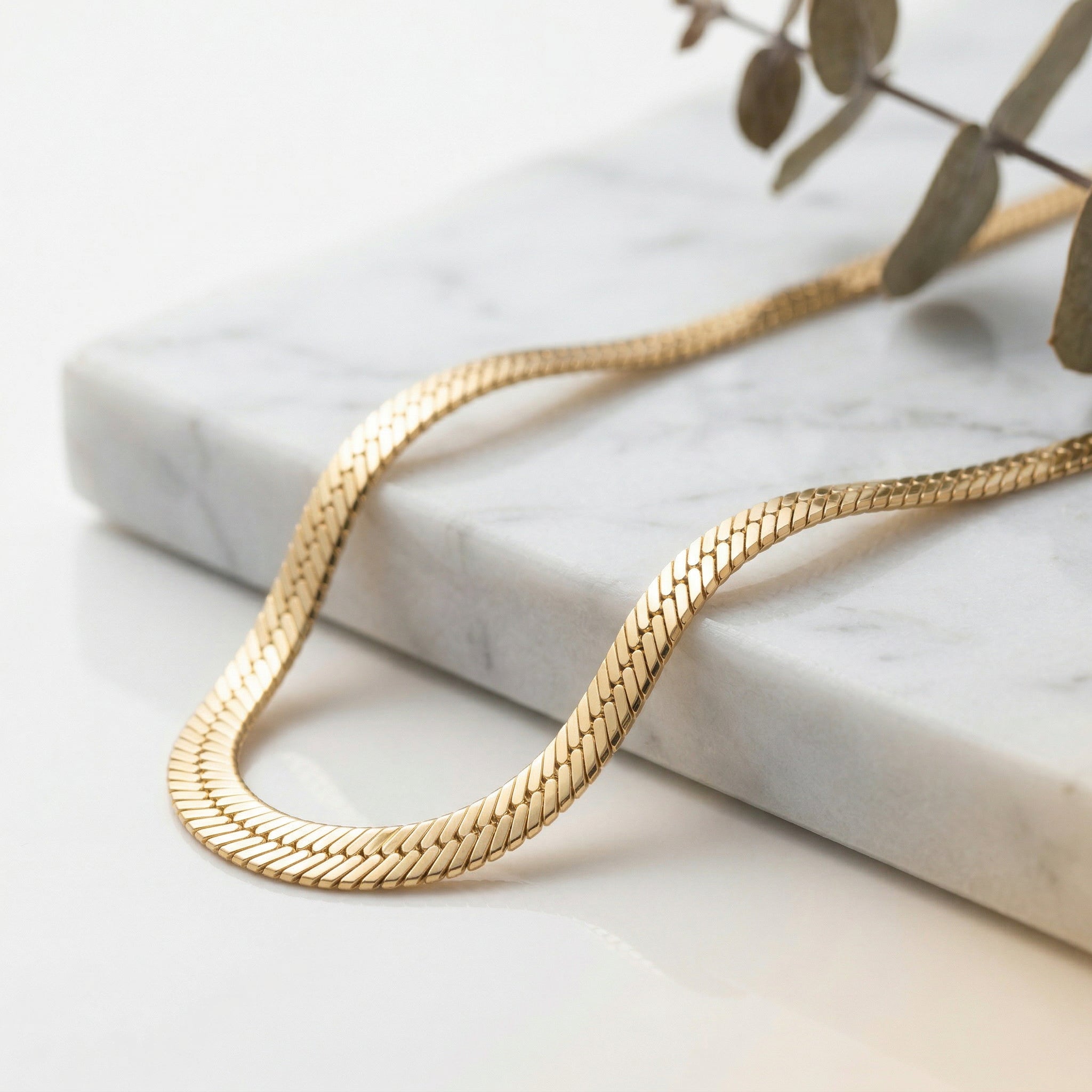 Gold-plated necklace on marble with eucalyptus