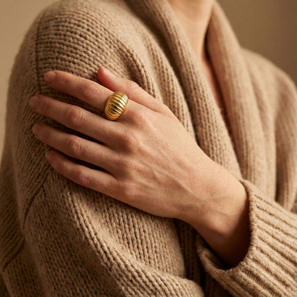 Model wearing a gold-plated twisted dome ring on her ring finger, with her hand resting on a beige knitted sweater.