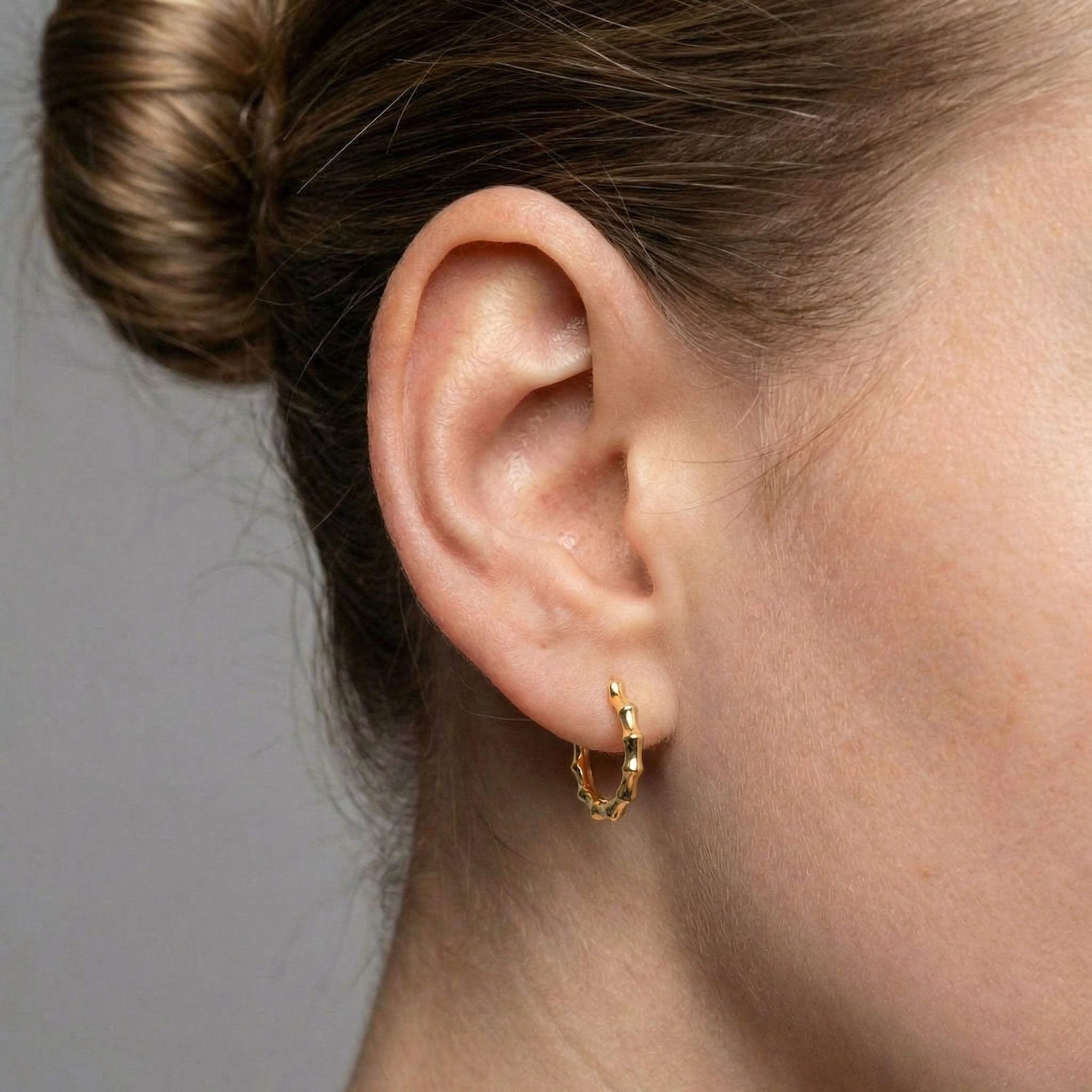 Gold-plated bamboo hoop earring worn on ear with hair up