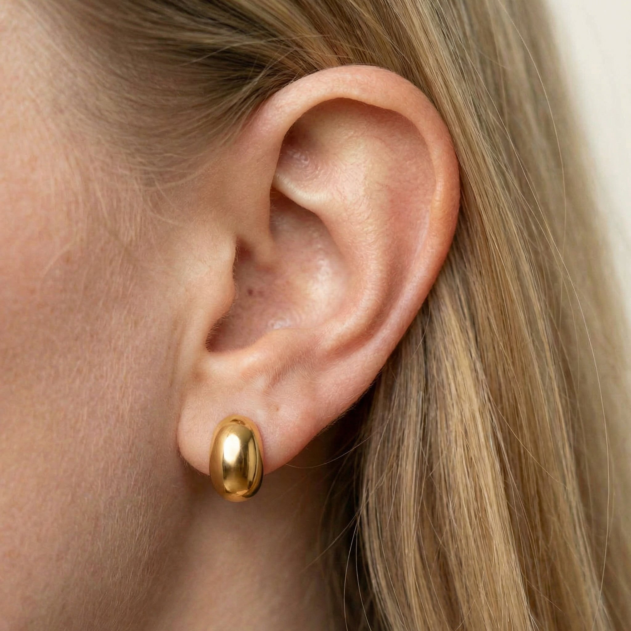Gold-plated bean stud earring on model's ear, close-up