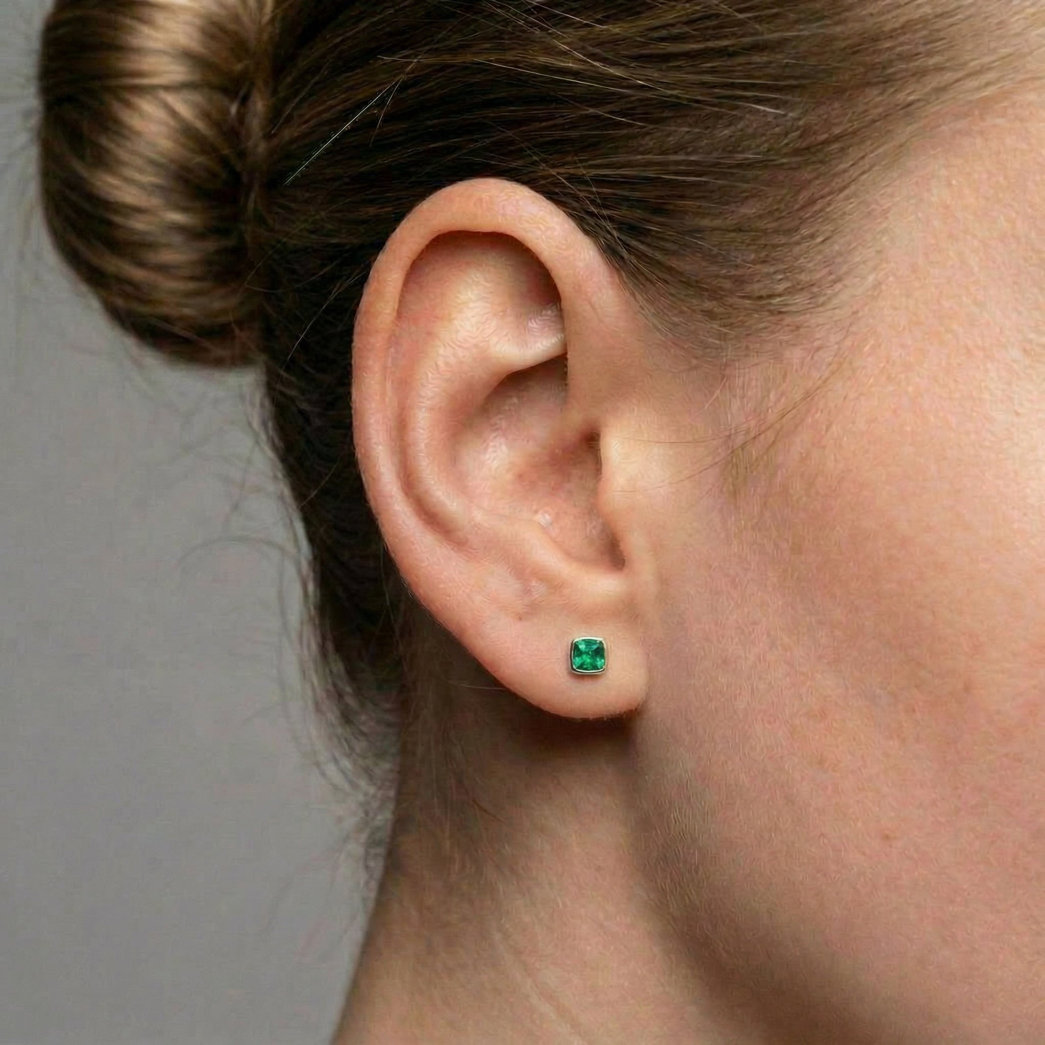 Model wearing a single square green stud earring in her earlobe, with hair pulled back.