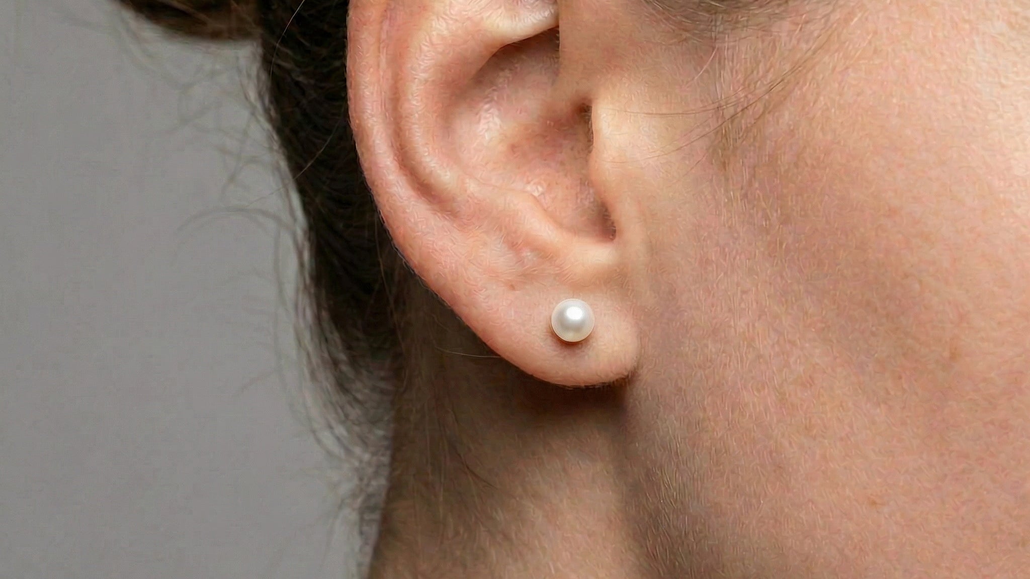 Gold-plated single pearl stud worn on ear