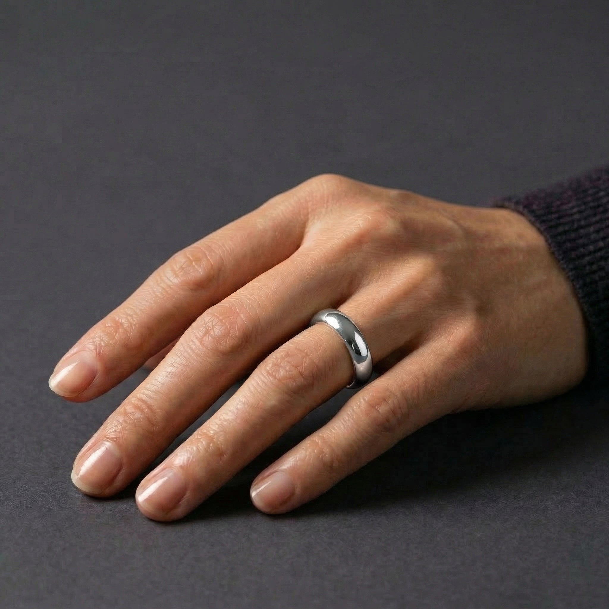 Silver ring worn on hand against dark background