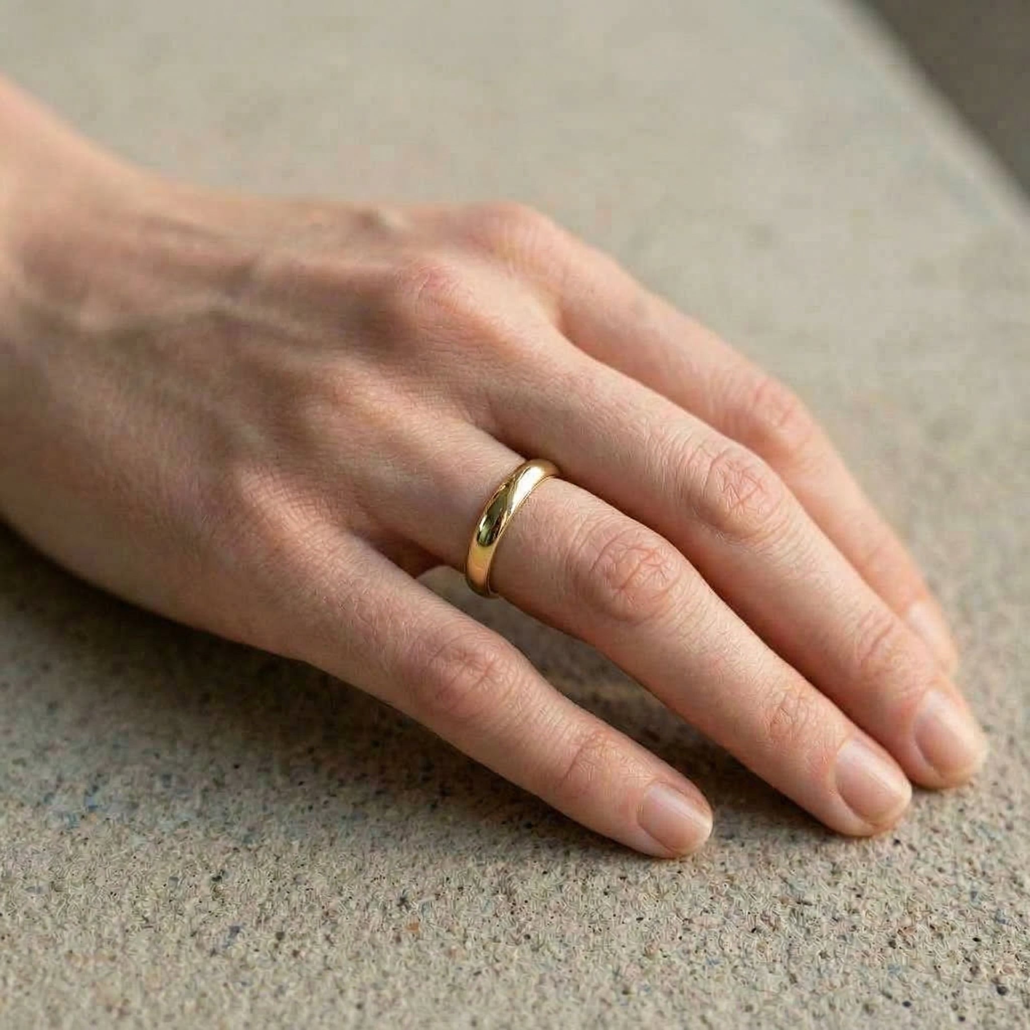 Gold-plated ring on hand, resting on concrete