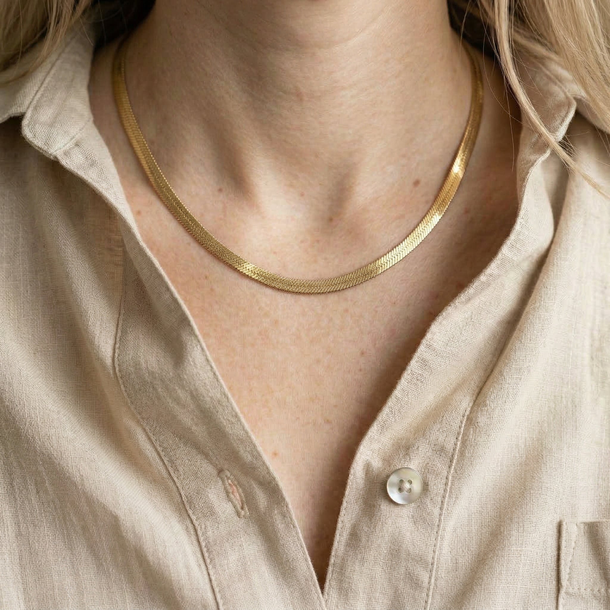 Model wearing a gold flat snake chain necklace with a beige linen shirt.