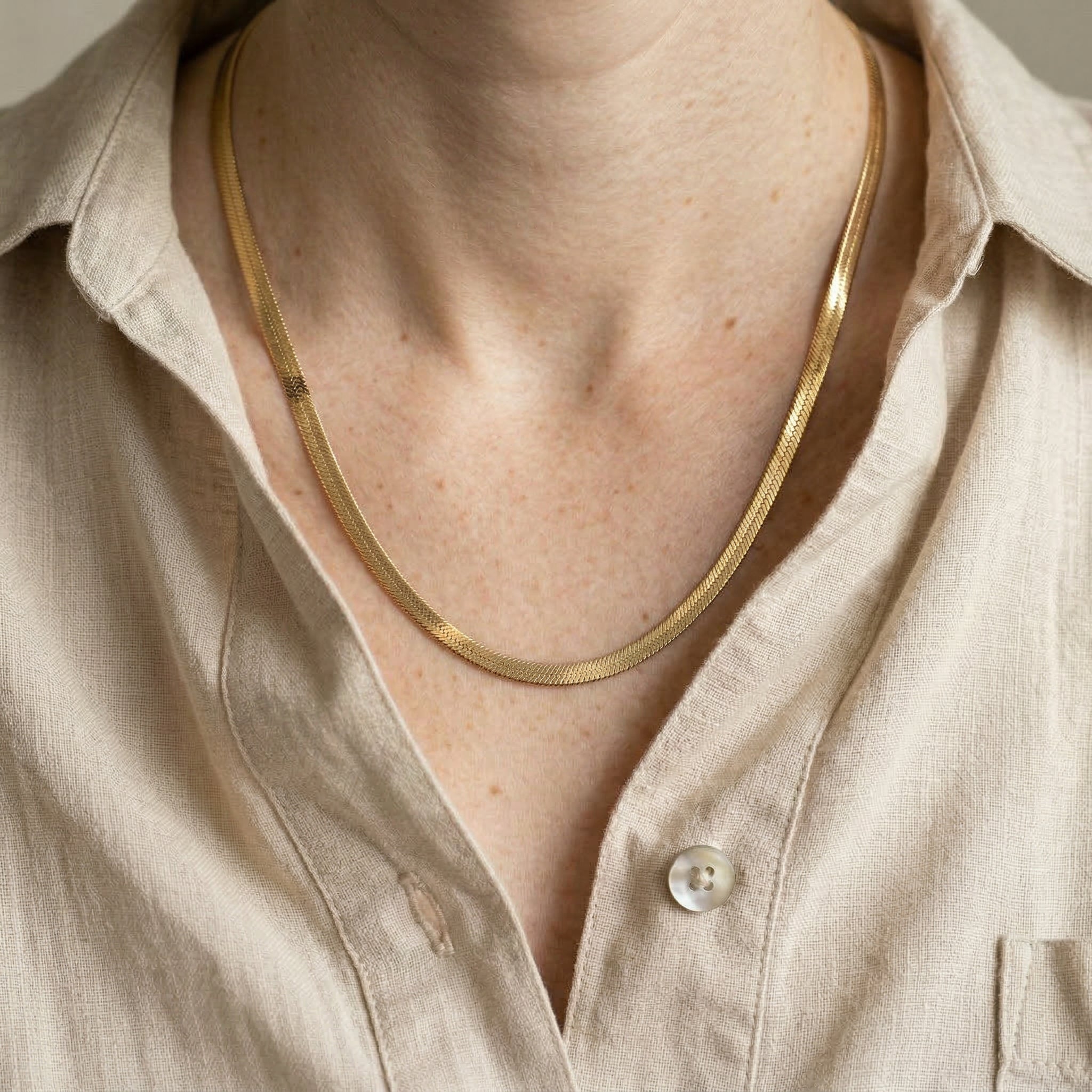 Model wearing a gold flat snake chain necklace with a light beige linen shirt.