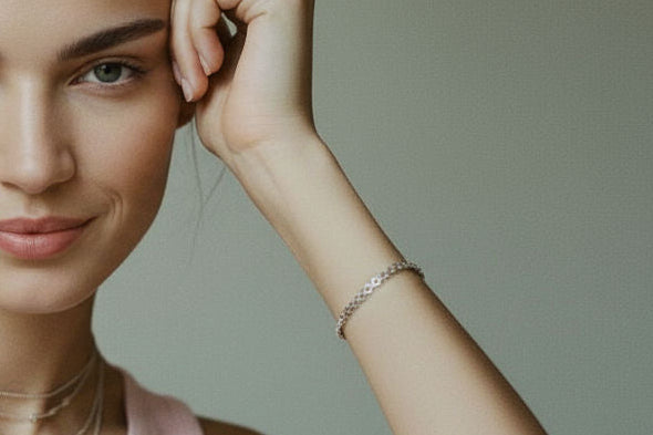 Woman wearing a silver chain bracelet with small circular links and layered silver necklaces, smiling slightly.