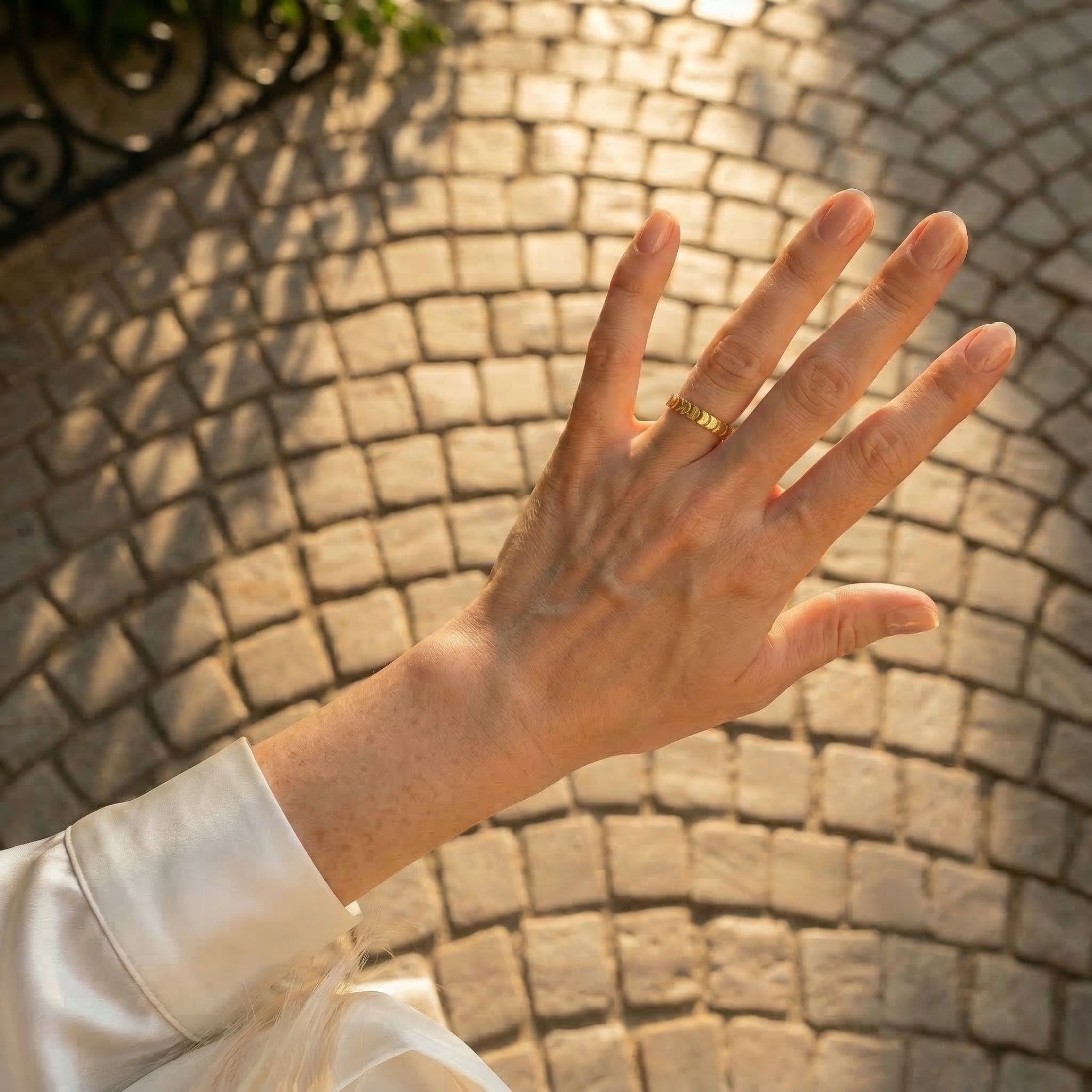 Gold-plated ring on hand over cobblestone background